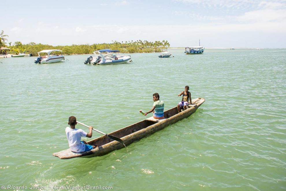 Imagem crianças no barco de madeira perto da lanchas na Praia da Boca da Barra.